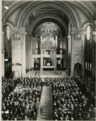 Large group at the pews, facing the front. Two are at the aisle's front