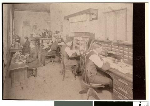 4 men and 2 women working on cluttered desks in the mill
