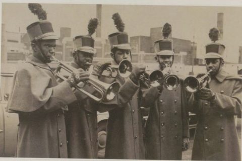 Photo of five young Black men playing trumpet in uniforms