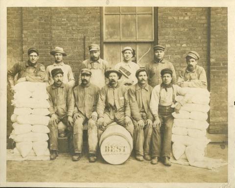 Group of flour mill employees with barrels and sacks of flour